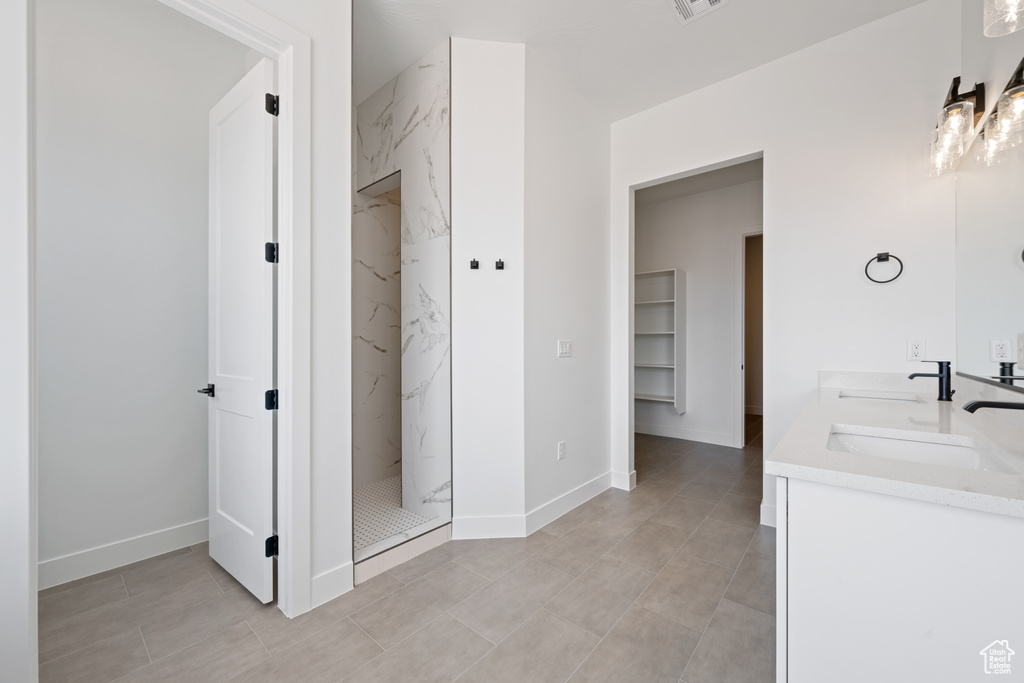 Bathroom featuring a marble finish shower, double vanity, and baseboards