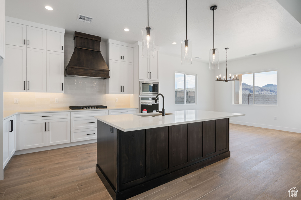 Kitchen featuring custom exhaust hood, stainless steel appliances, a sink, light wood-type flooring, and light countertops