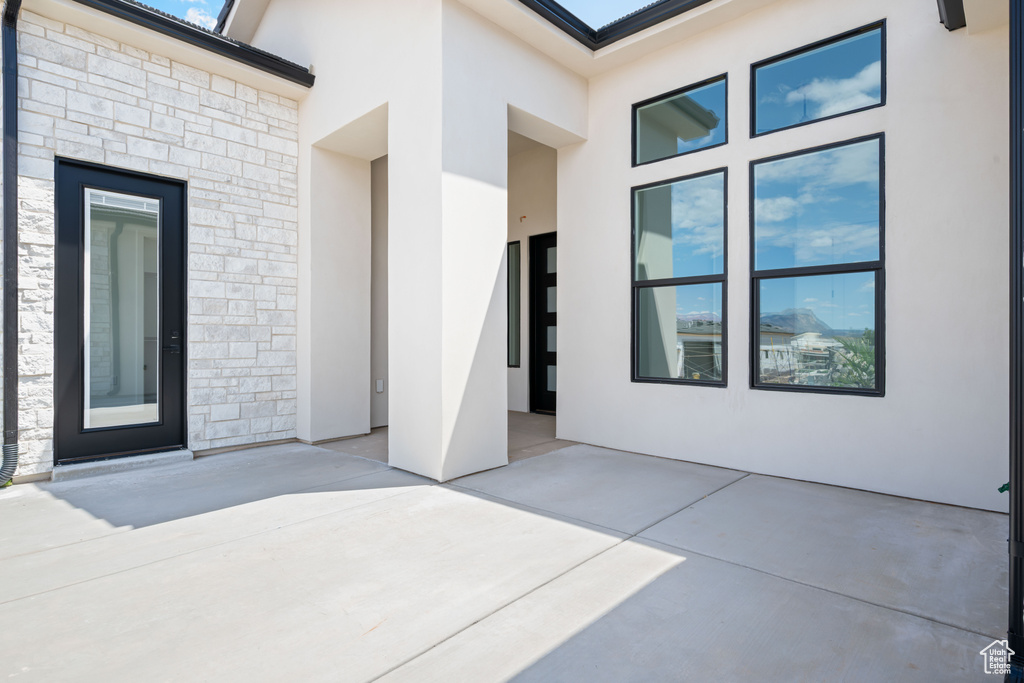 Doorway to property featuring stone siding, stucco siding, and a patio area