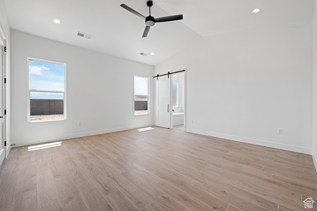 Unfurnished bedroom featuring a barn door, light wood-style floors, lofted ceiling, recessed lighting, and baseboards