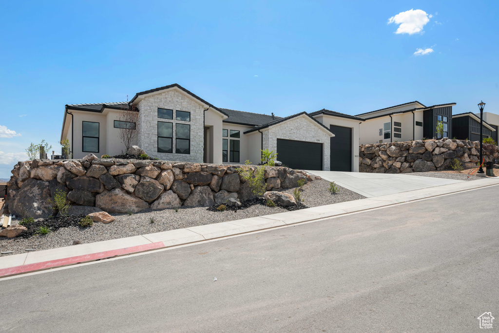 Contemporary house featuring an attached garage, stone siding, concrete driveway, and stucco siding