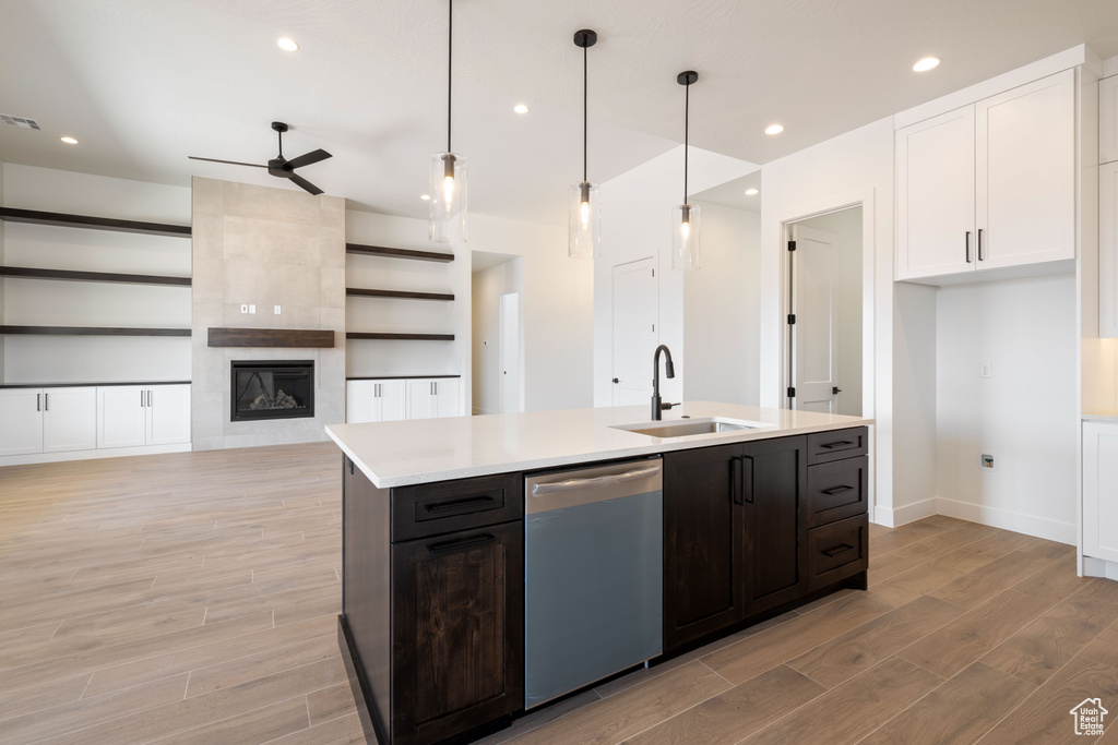 Kitchen with stainless steel dishwasher, a sink, ceiling fan, light wood-style floors, and light countertops