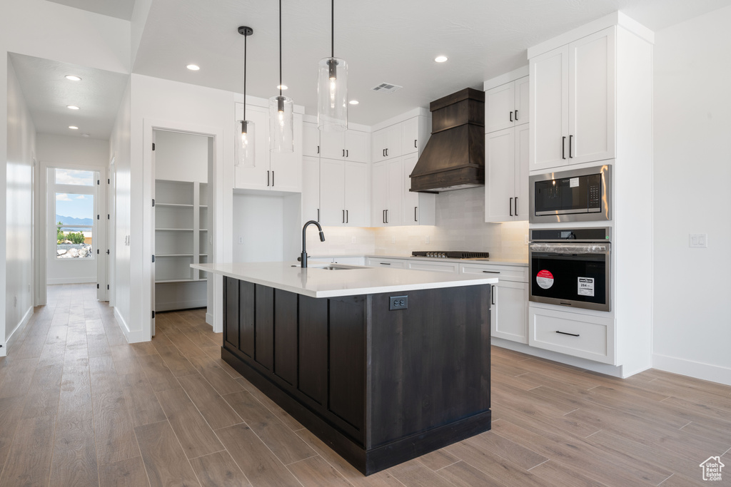 Kitchen featuring stainless steel appliances, a sink, custom range hood, baseboards, and light wood finished floors