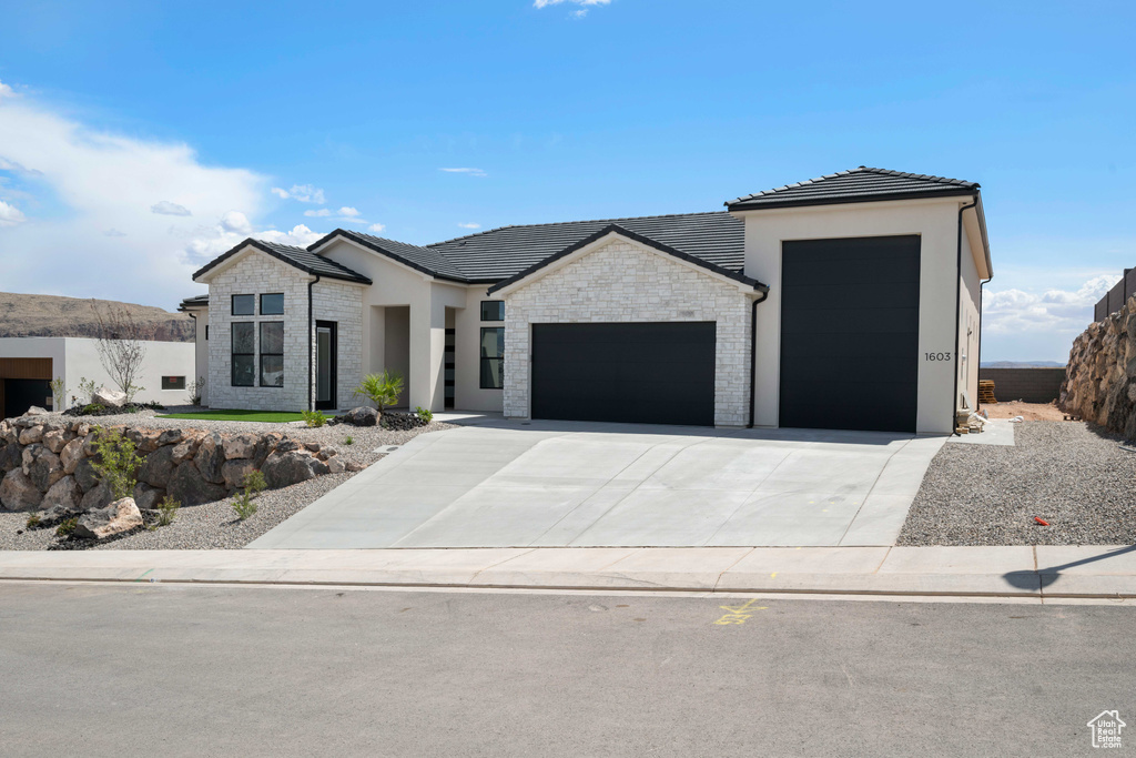 Contemporary home featuring an attached garage, concrete driveway, stone siding, and stucco siding