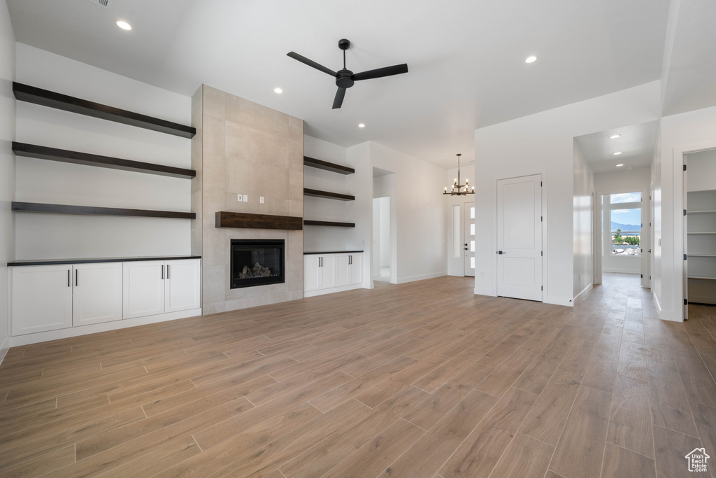 Unfurnished living room featuring ceiling fan, a chandelier, light wood-style floors, a tiled fireplace, and recessed lighting