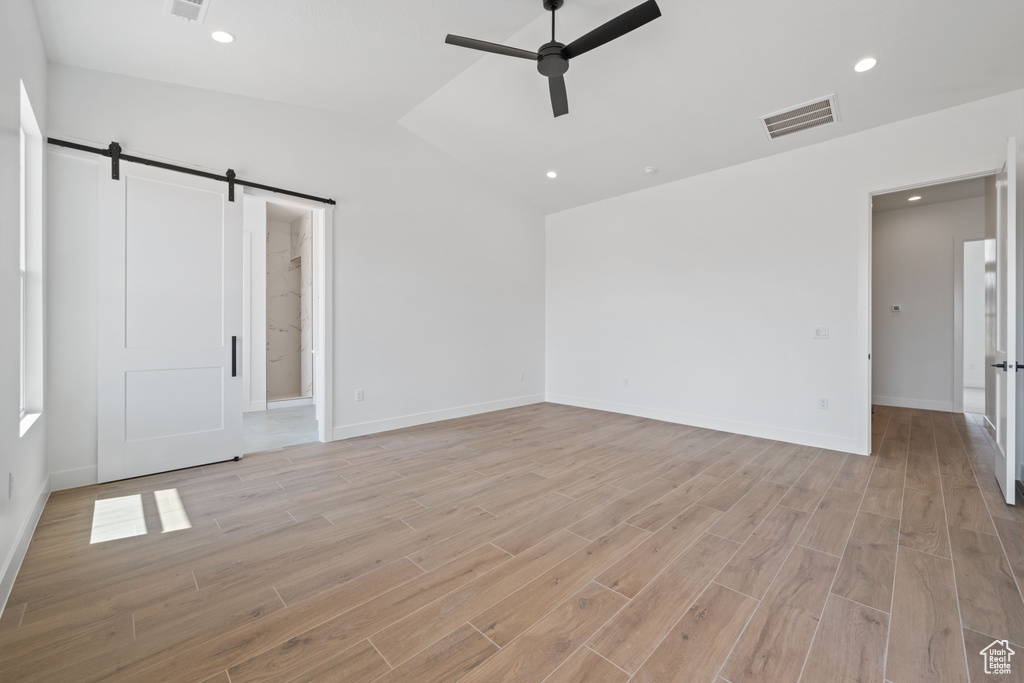 Unfurnished bedroom with a barn door, light wood finished floors, baseboards, vaulted ceiling, and recessed lighting