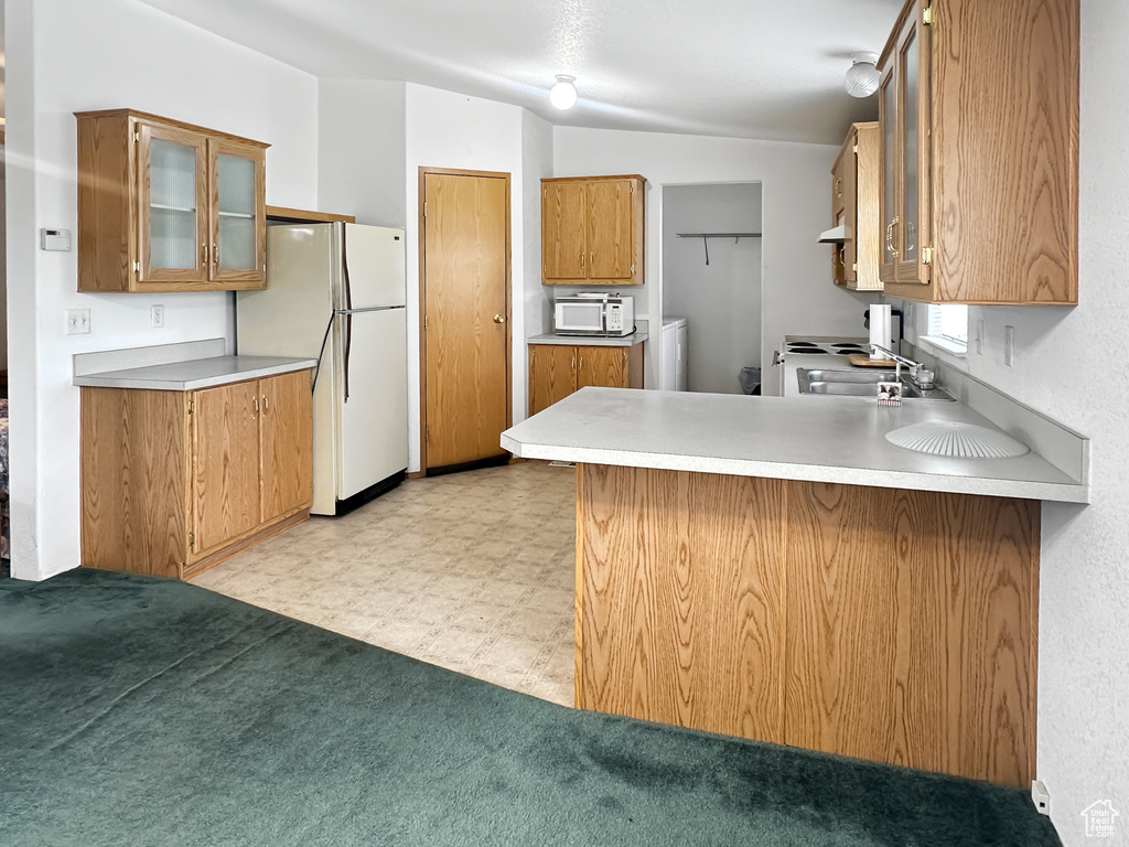 Kitchen featuring white appliances, a peninsula, brown cabinetry, glass insert cabinets, and a sink
