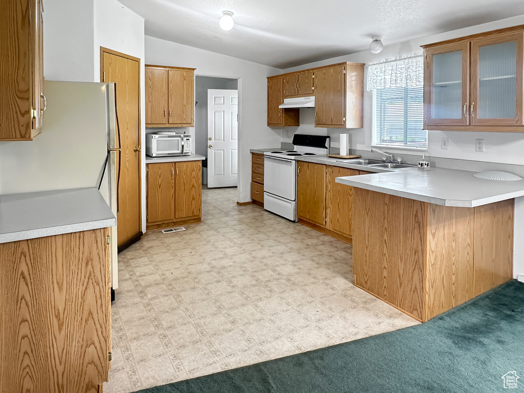 Kitchen featuring white appliances, a peninsula, a sink, under cabinet range hood, and brown cabinetry