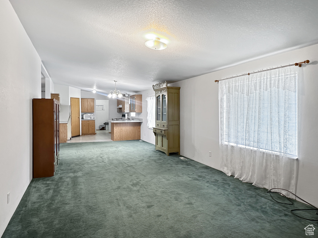 Unfurnished living room featuring lofted ceiling, a textured ceiling, a chandelier, and carpet floors