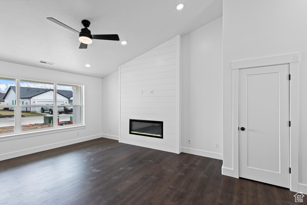 Unfurnished living room featuring vaulted ceiling, wood finished floors, ceiling fan, a large fireplace, and baseboards
