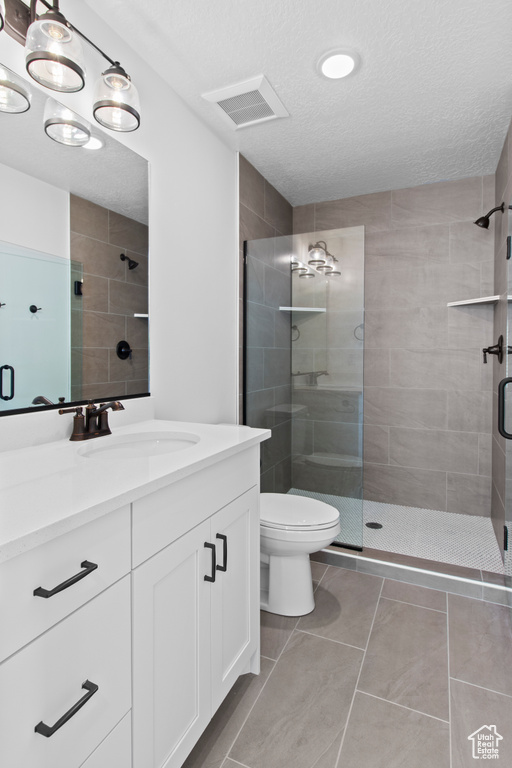 Full bathroom featuring a shower stall, a textured ceiling, toilet, vanity, and tile patterned flooring