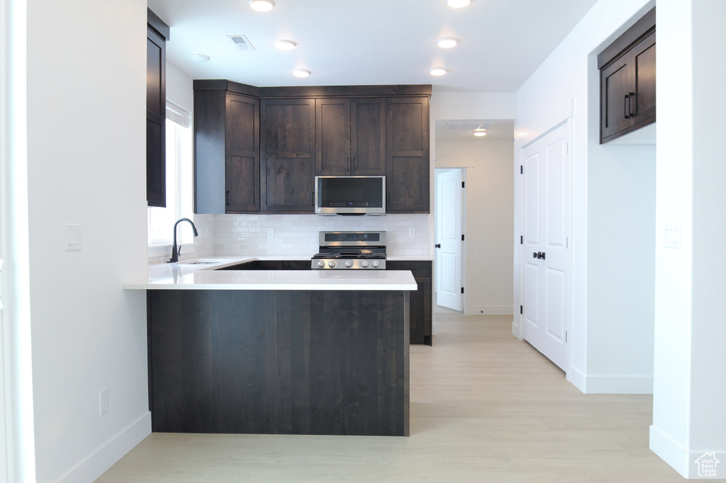 Kitchen featuring range, stainless steel microwave, dark brown cabinets, backsplash, and light countertops
