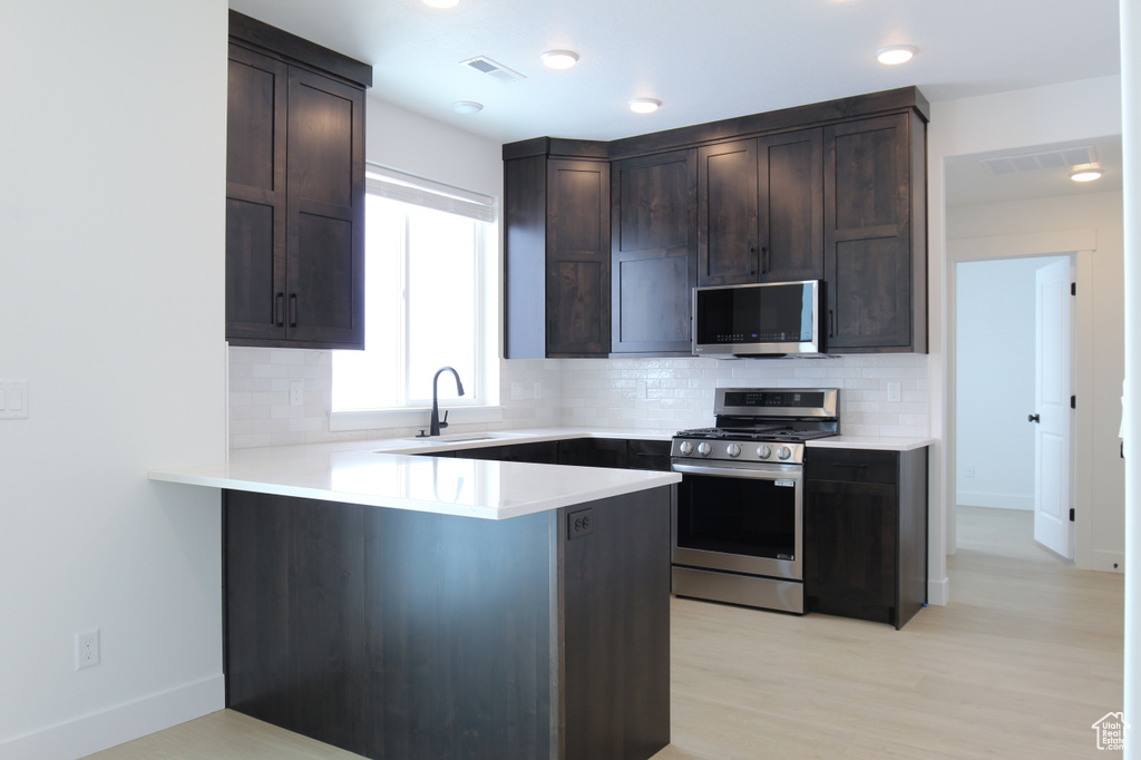 Kitchen featuring stainless steel appliances, a sink, dark brown cabinets, decorative backsplash, and a peninsula