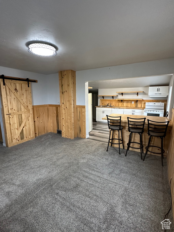 Carpeted dining room featuring a barn door, wainscoting, and wood walls