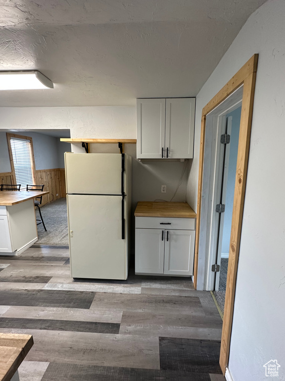 Kitchen with freestanding refrigerator, light wood-style flooring, wainscoting, white cabinets, and wood walls