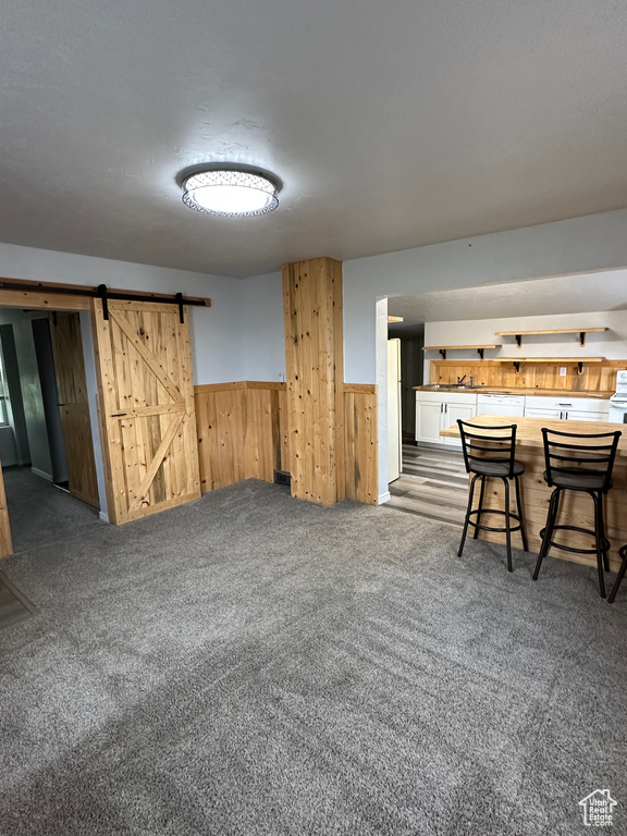 Basement featuring wood walls, carpet flooring, a barn door, and wainscoting