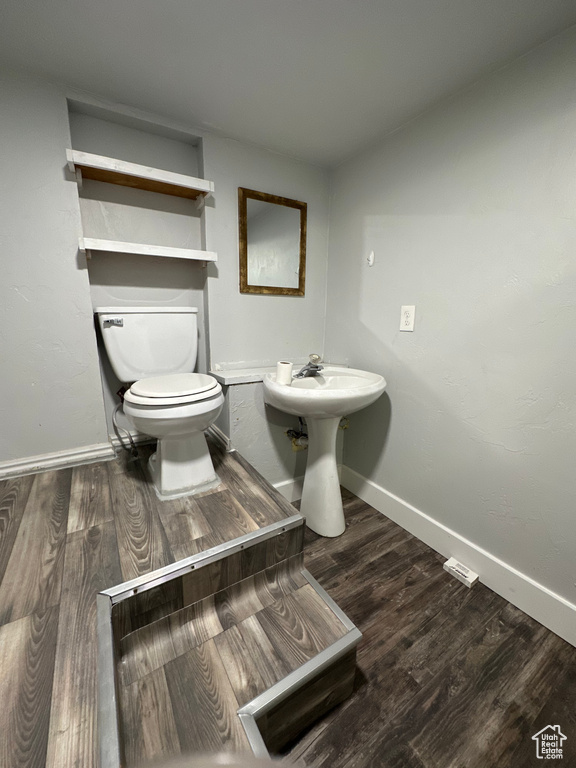 Half bathroom with baseboards, toilet, wood finished floors, and a sink