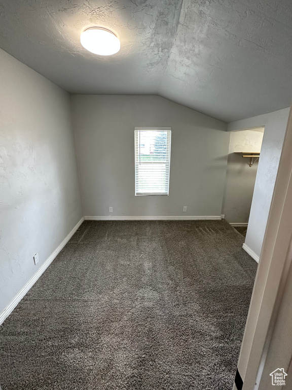 Unfurnished room with vaulted ceiling, a textured ceiling, dark colored carpet, and baseboards