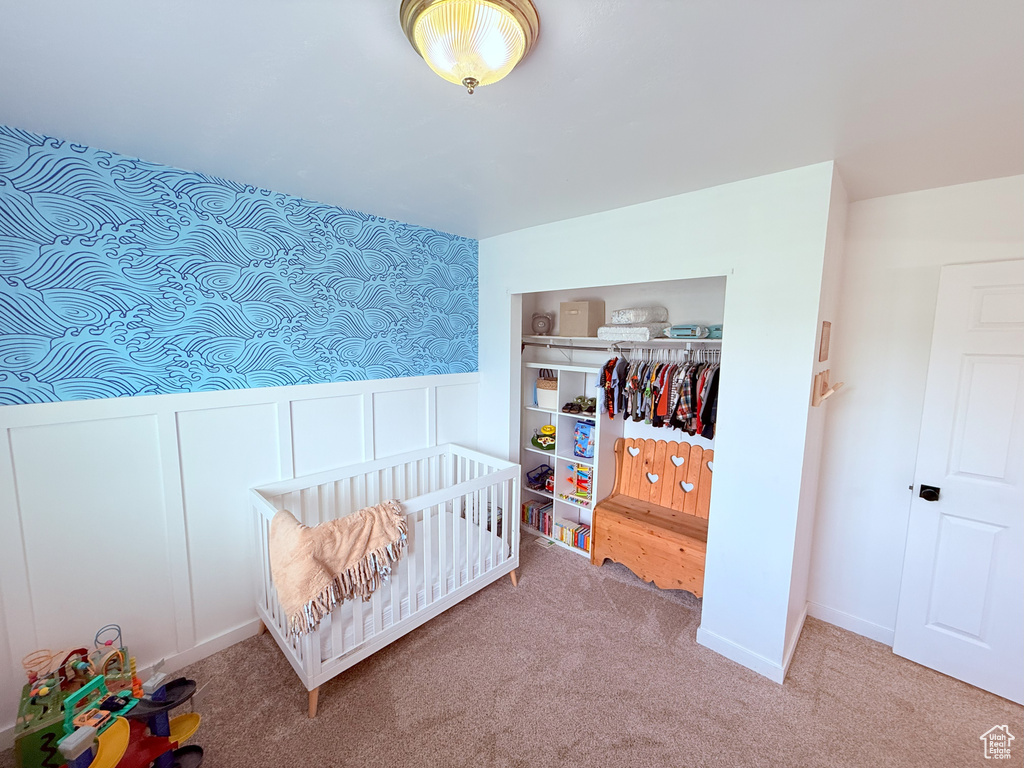 Bedroom featuring a closet, carpet floors, wainscoting, a decorative wall, and a crib