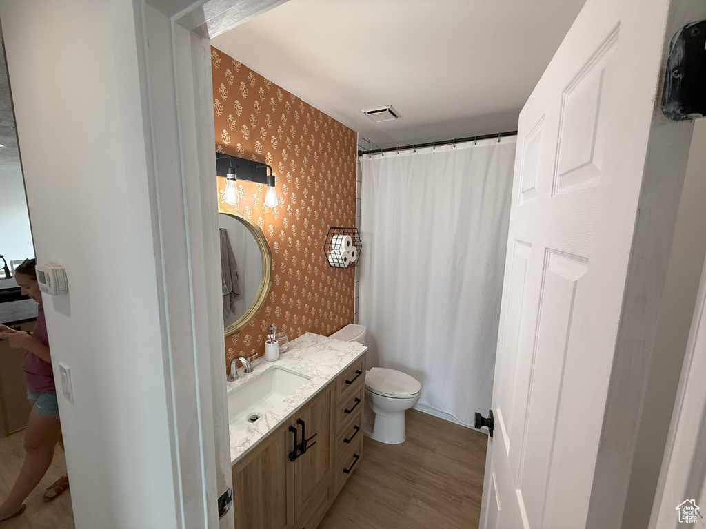 Full bathroom with wallpapered walls, wood finished floors, vanity, toilet, and a shower with curtain