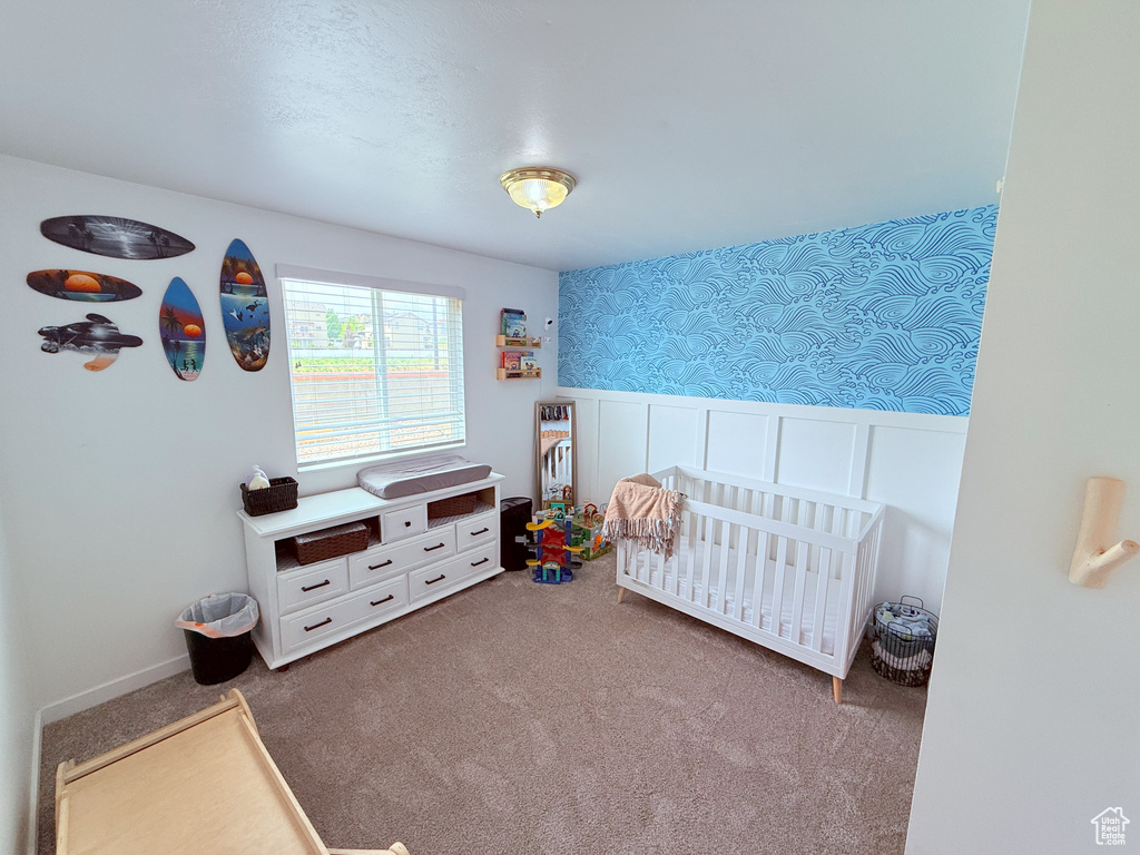 Bedroom with wallpapered walls, carpet flooring, a wainscoted wall, a crib, and a decorative wall