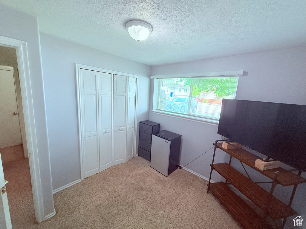 Bedroom featuring light colored carpet, a closet, a textured ceiling, fridge, and baseboards