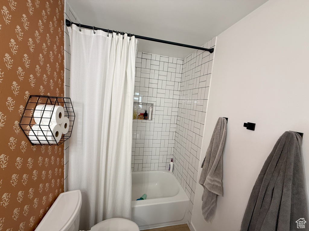 Full bathroom featuring wallpapered walls, toilet, and shower / bathtub combination with curtain