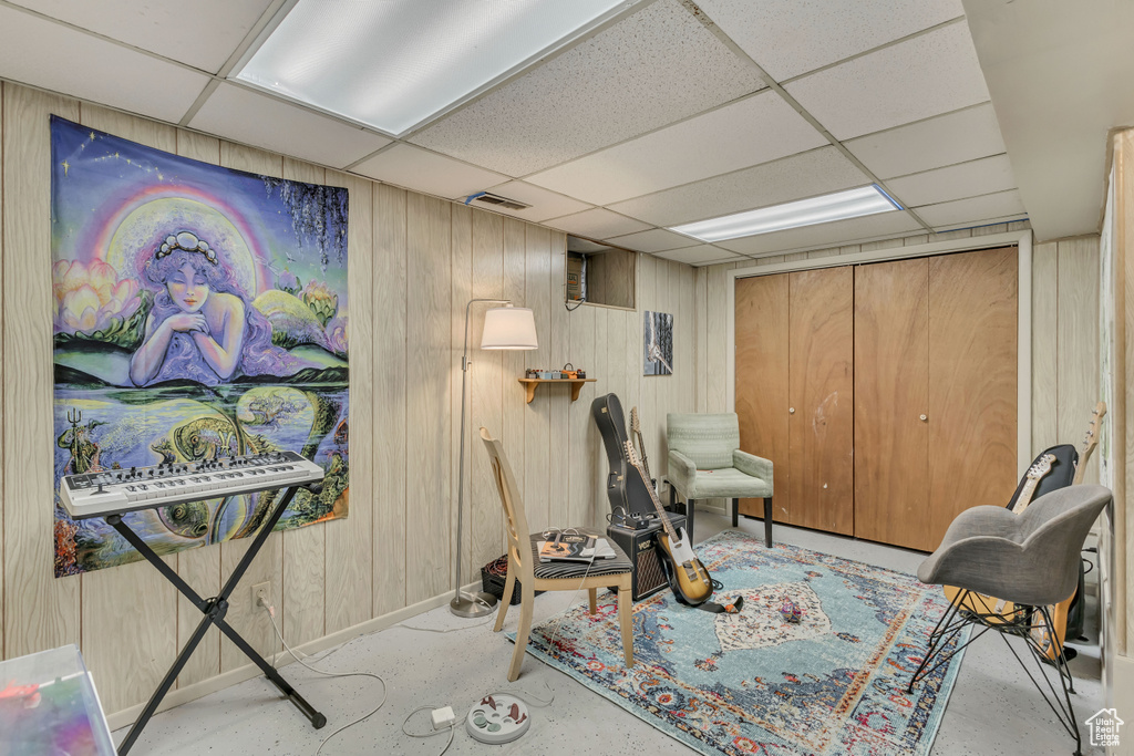 Living area with a drop ceiling, baseboards, wooden walls, and concrete floors