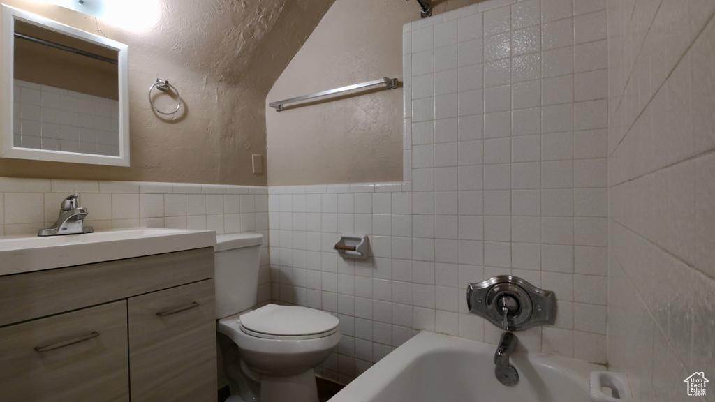 Bathroom with tile walls, a textured wall, toilet, vanity, and wainscoting