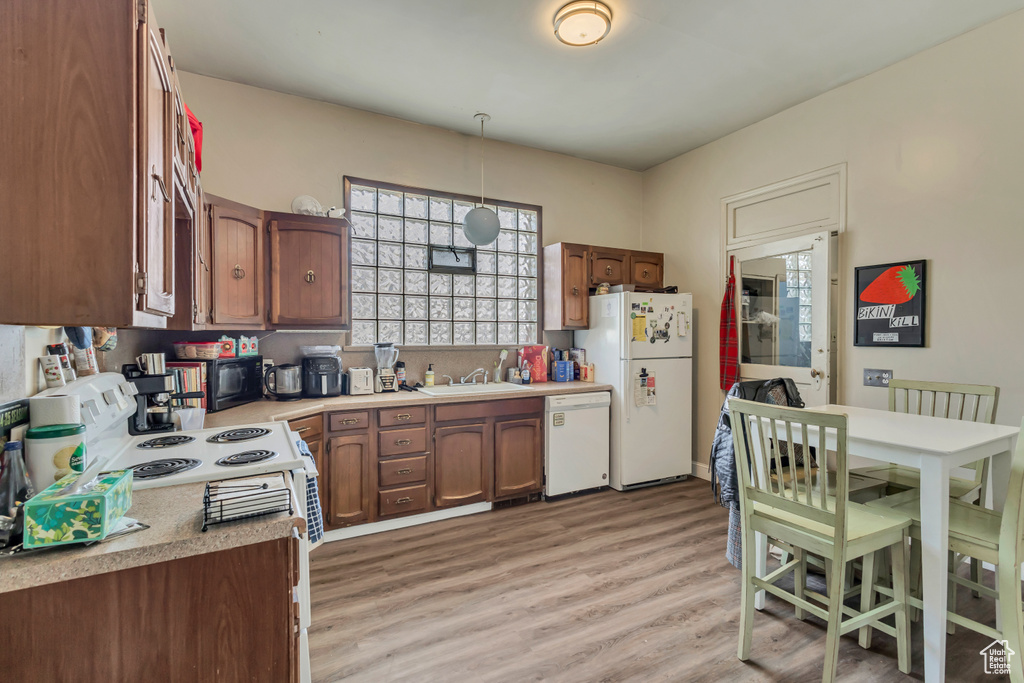 Kitchen with white appliances, light countertops, light wood-style flooring, decorative light fixtures, and a sink