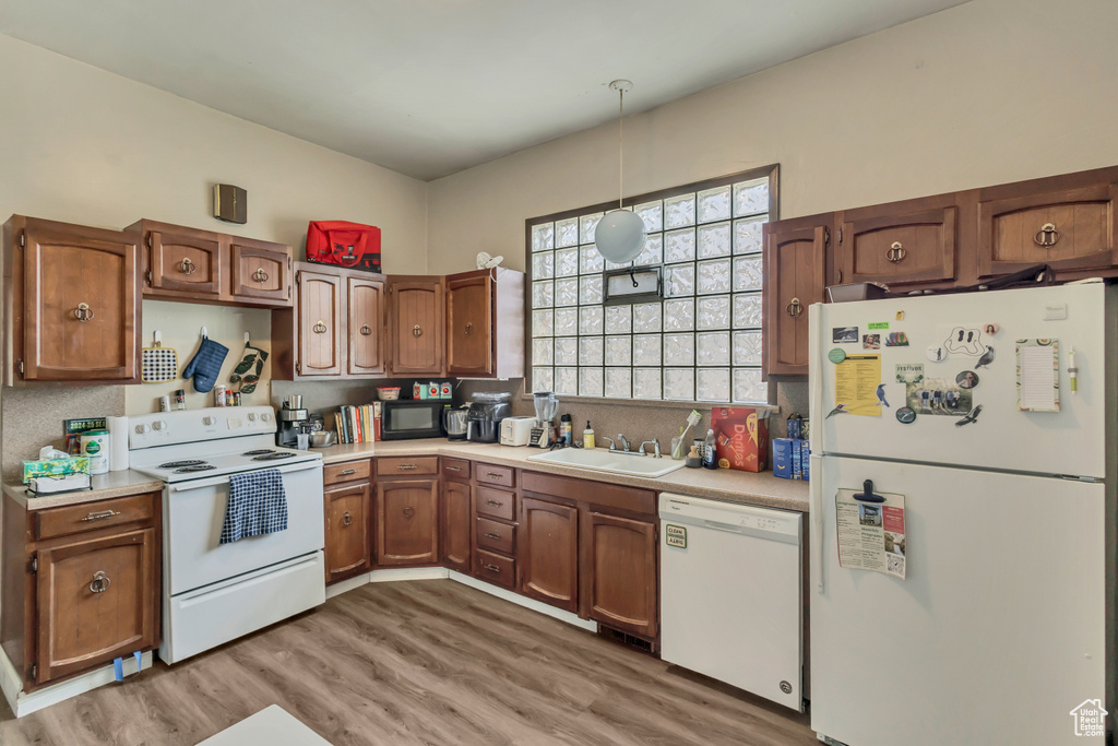 Kitchen with white appliances, a sink, light countertops, and light wood-type flooring