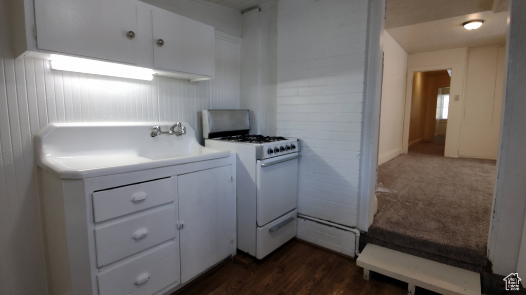 Kitchen with white range with gas stovetop, white cabinetry, dark wood-style flooring, and light countertops