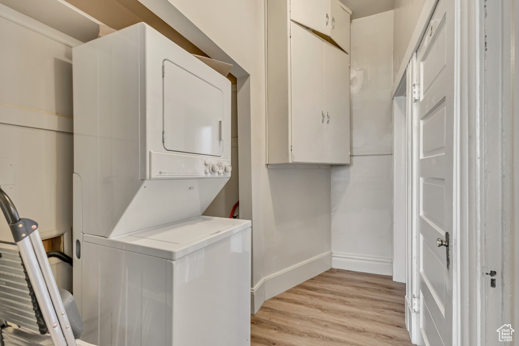 Washroom with stacked washing machine and dryer, light wood-style floors, and baseboards