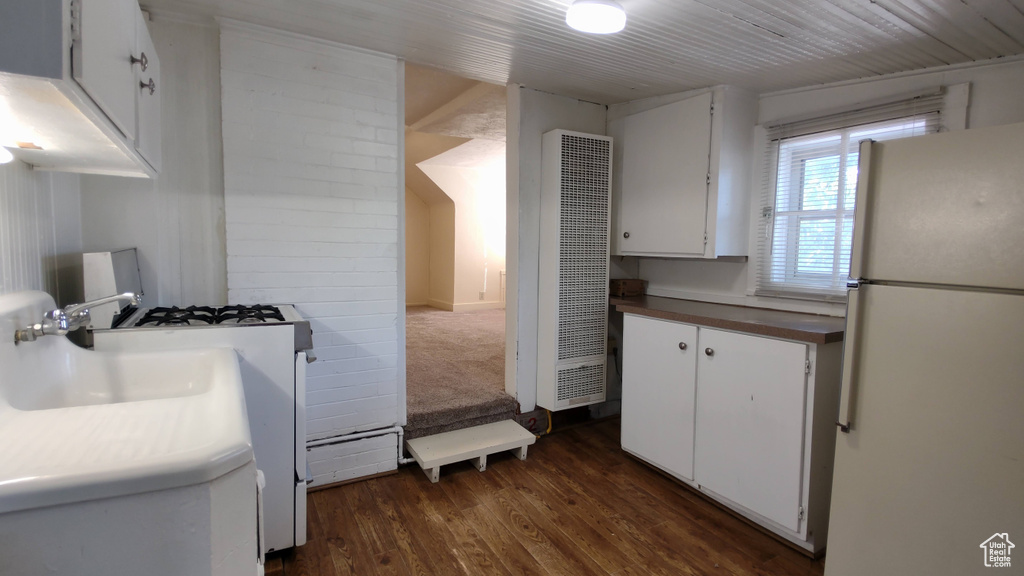Kitchen with white appliances, a heating unit, dark wood-type flooring, white cabinets, and a sink