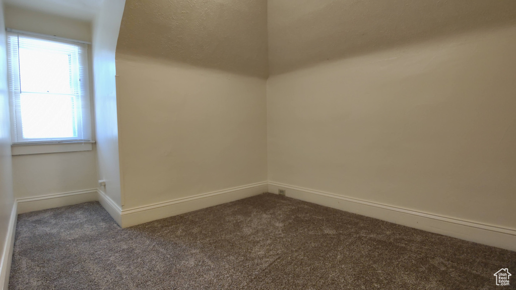 Empty room featuring dark colored carpet, plenty of natural light, and baseboards