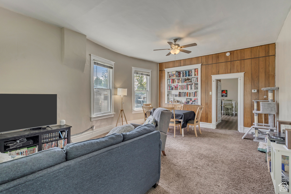 Carpeted living room featuring a ceiling fan and wood walls