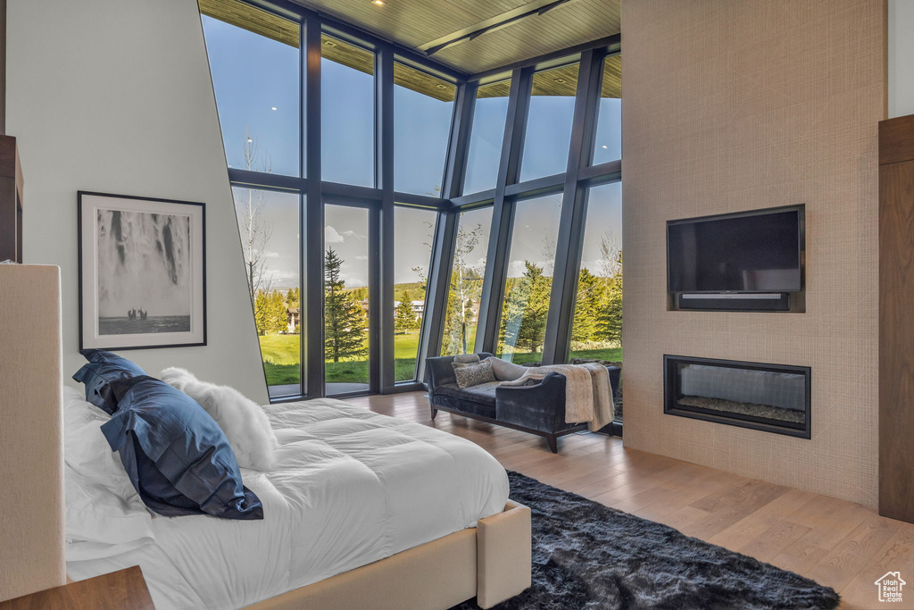 Bedroom with a towering ceiling, a glass covered fireplace, wood finished floors, multiple windows, and expansive windows