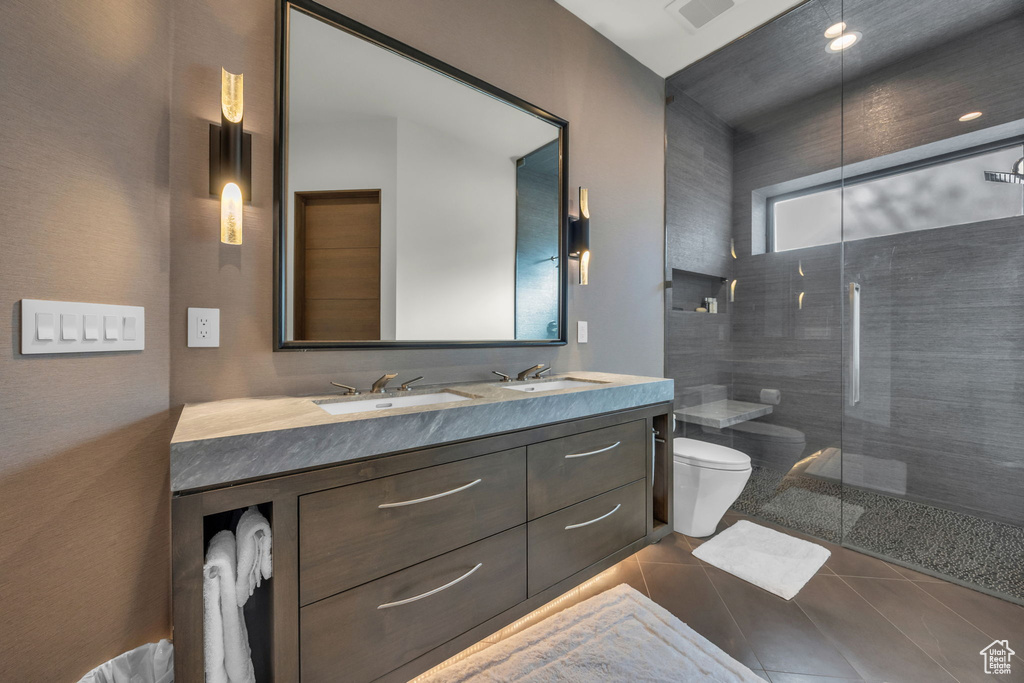 Full bathroom featuring toilet, a tile shower, tile patterned flooring, and double vanity