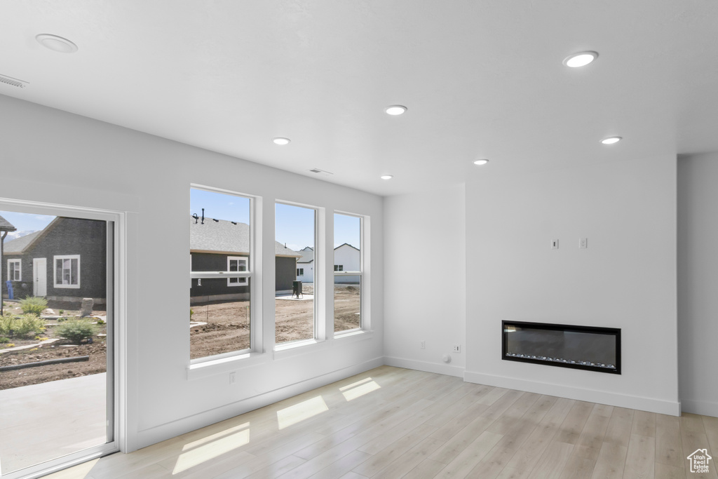 Unfurnished living room featuring light wood-style floors, recessed lighting, a glass covered fireplace, and baseboards