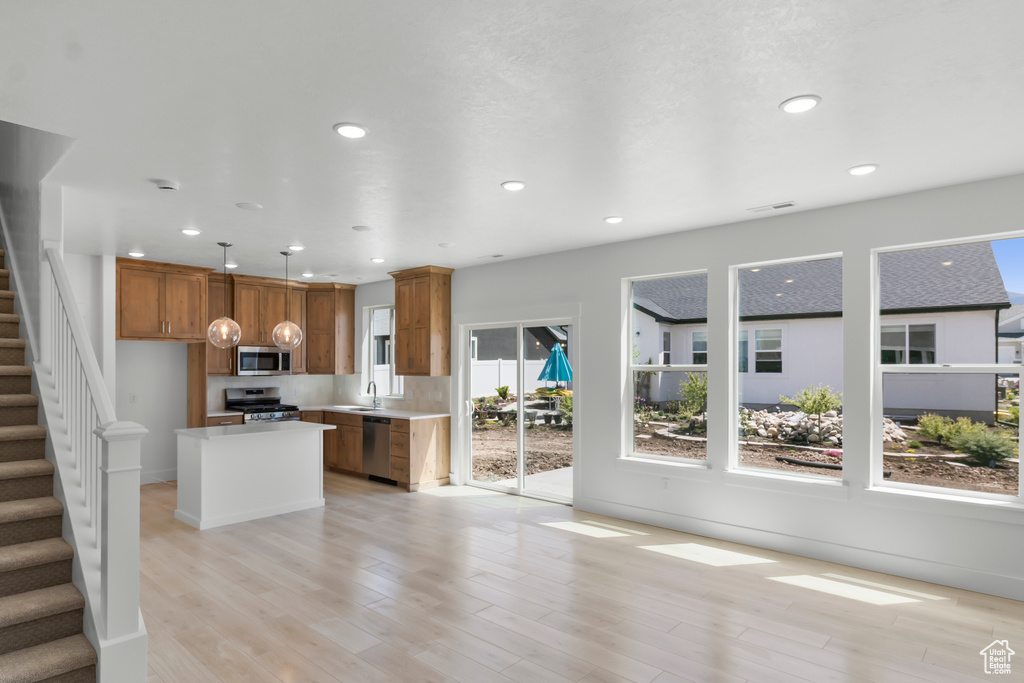 Kitchen featuring stainless steel appliances, brown cabinets, light countertops, light wood-style flooring, and a kitchen island