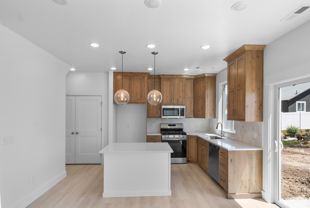 Kitchen with appliances with stainless steel finishes, a sink, light wood-type flooring, tasteful backsplash, and recessed lighting