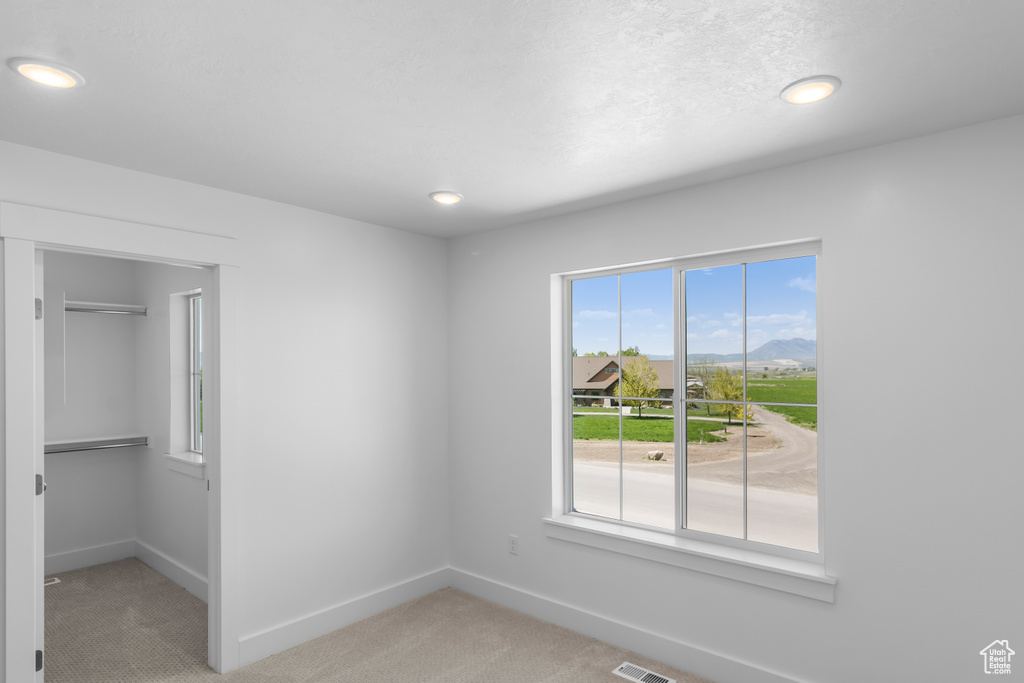Unfurnished bedroom with light colored carpet, baseboards, a spacious closet, and recessed lighting