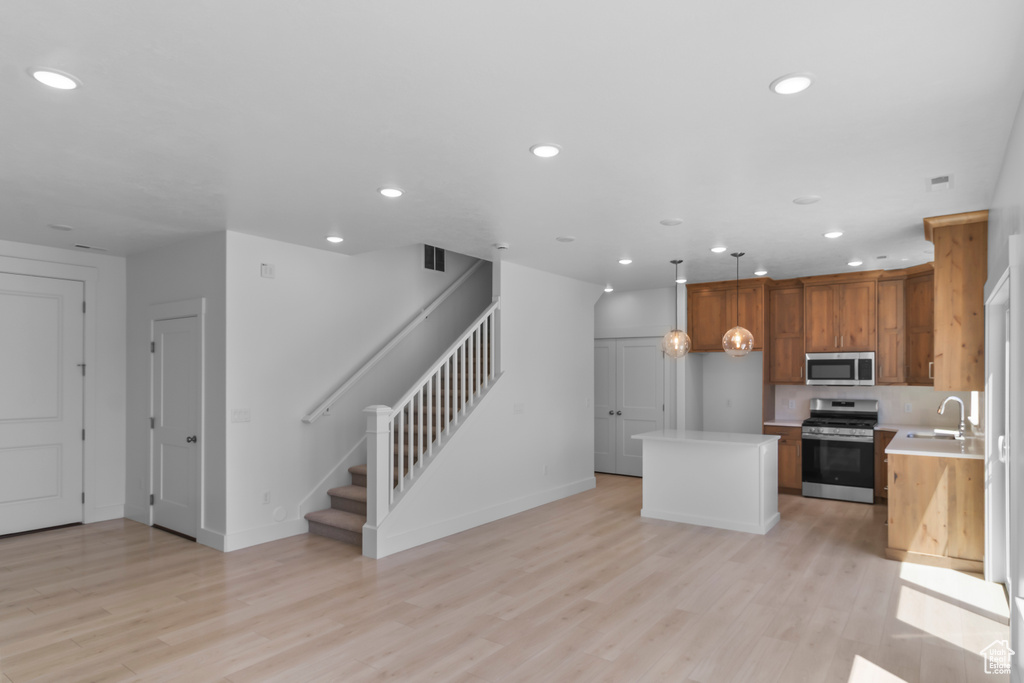 Kitchen with appliances with stainless steel finishes, a sink, light countertops, a kitchen island, and light wood finished floors