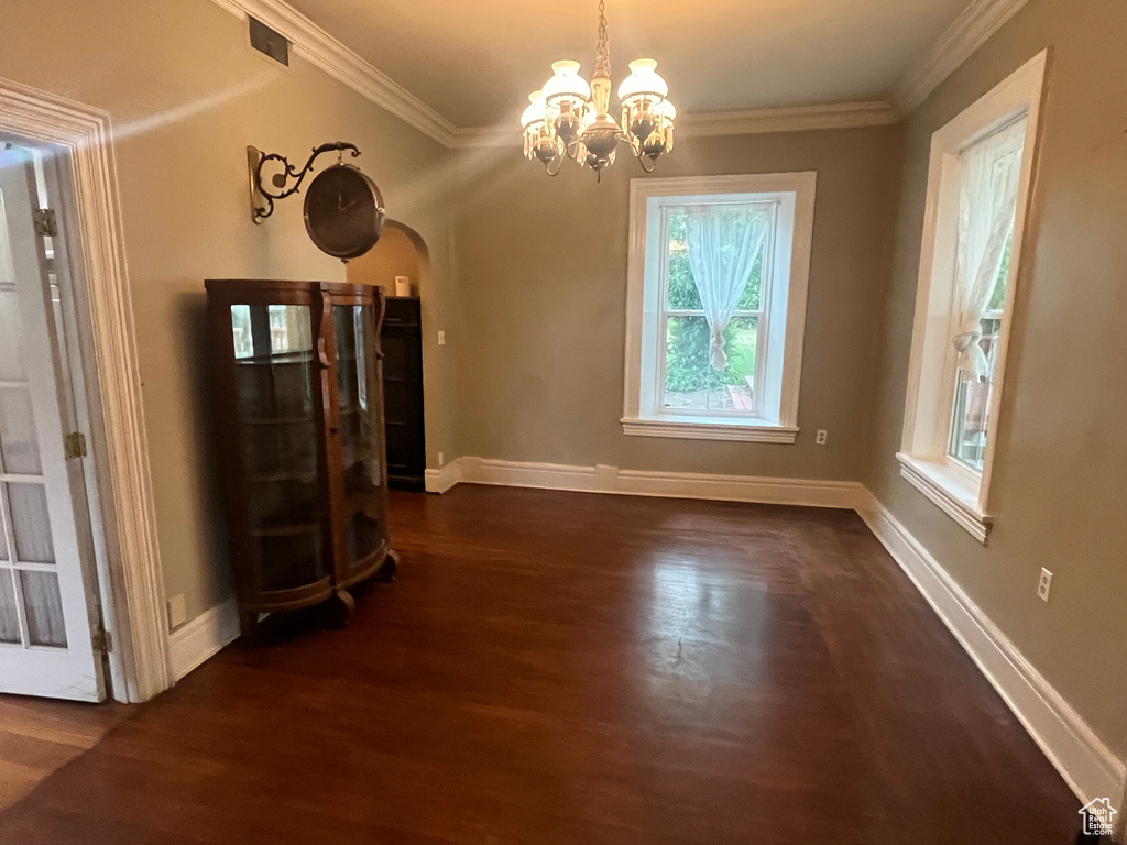 Unfurnished dining area featuring dark wood-type flooring, arched walkways, a chandelier, ornamental molding, and baseboards