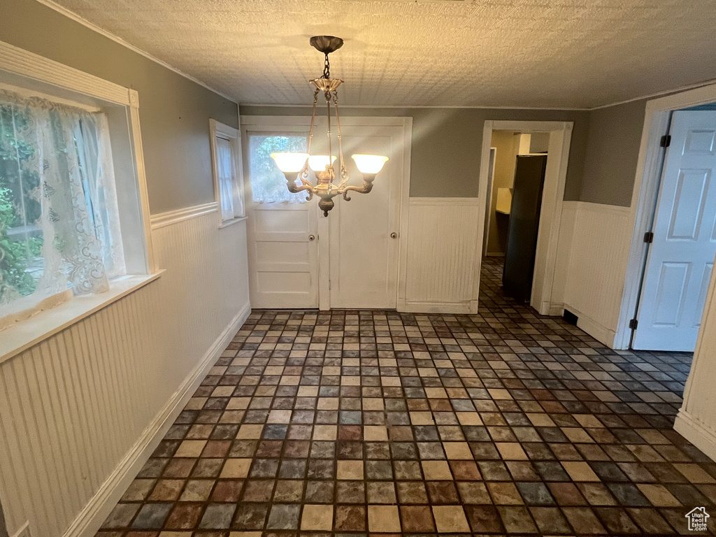 Unfurnished dining area with wainscoting, a chandelier, a textured ceiling, ornamental molding, and baseboards