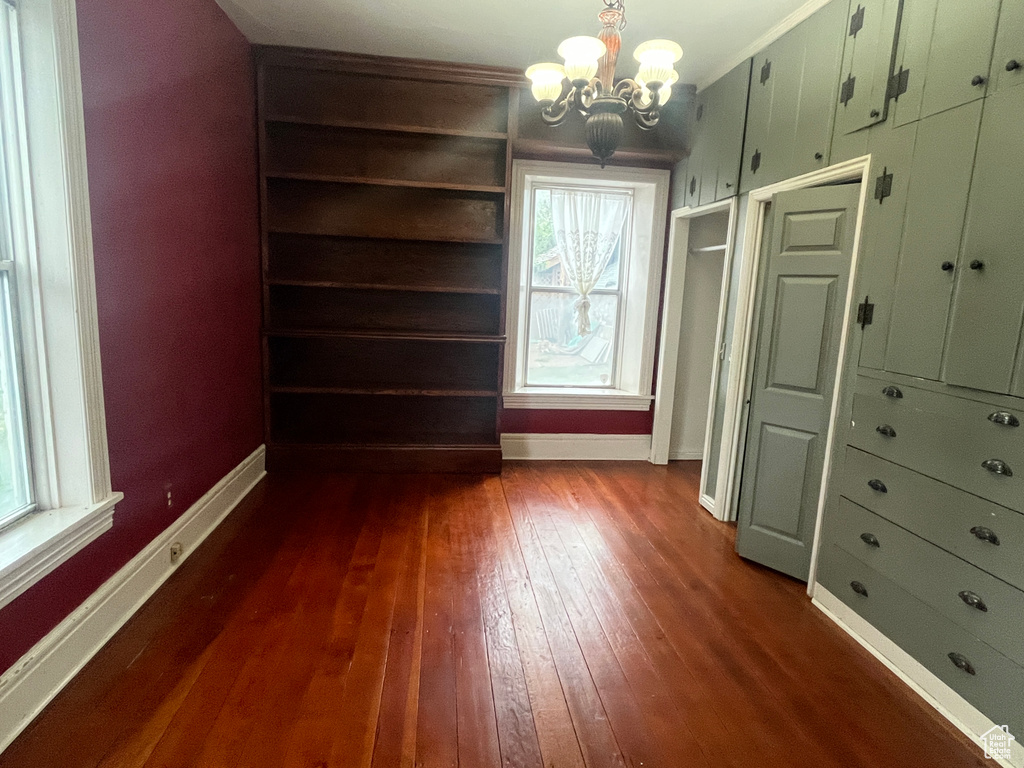 Unfurnished dining area featuring dark wood-style floors, a chandelier, baseboards, plenty of natural light, and crown molding