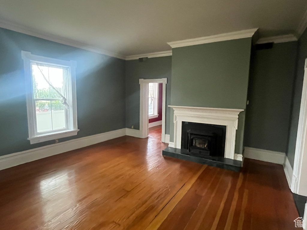Unfurnished living room featuring healthy amount of natural light, wood finished floors, ornamental molding, and baseboards