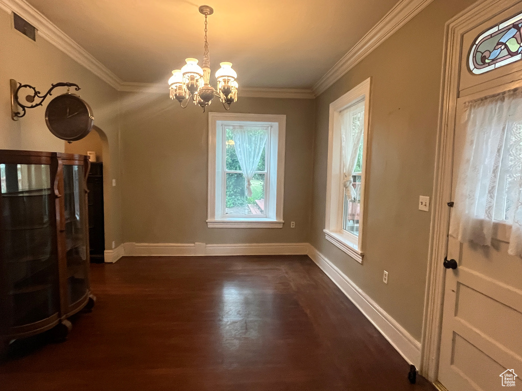 Unfurnished living room featuring arched walkways, a chandelier, dark wood finished floors, crown molding, and baseboards