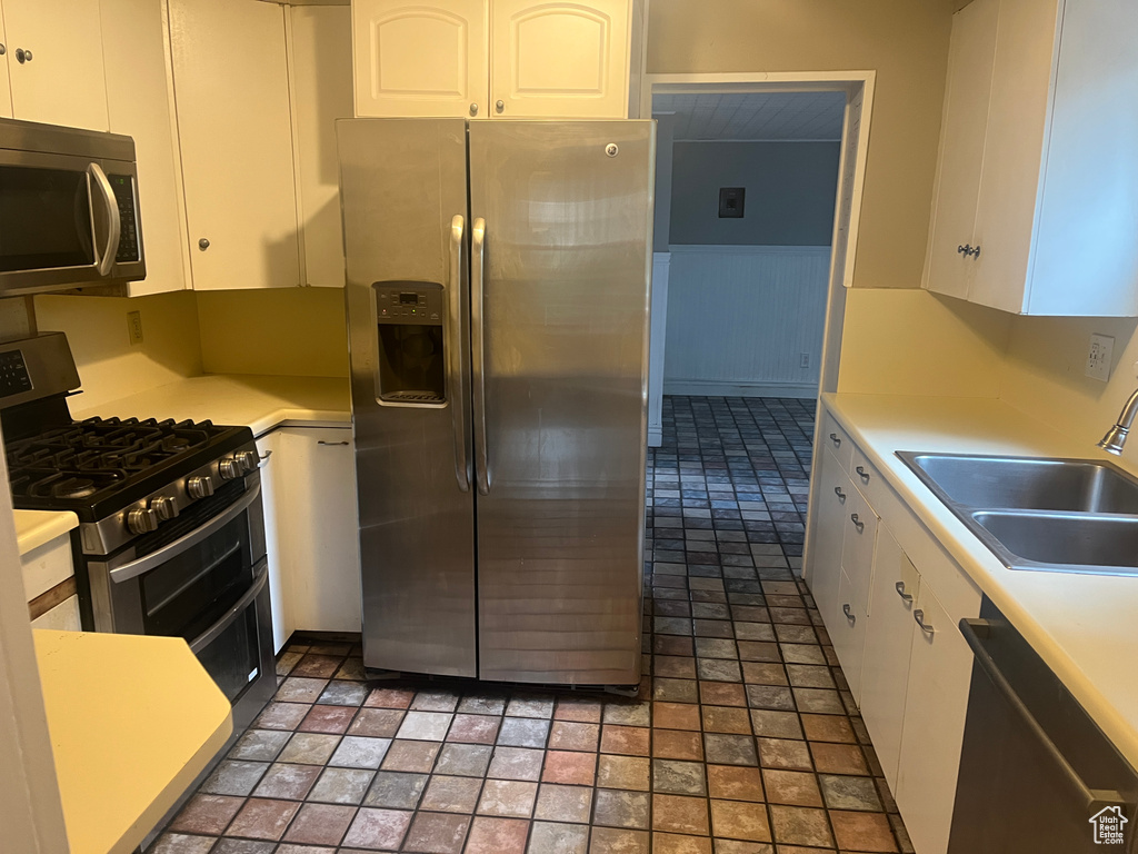 Kitchen with appliances with stainless steel finishes, a sink, white cabinets, and light countertops