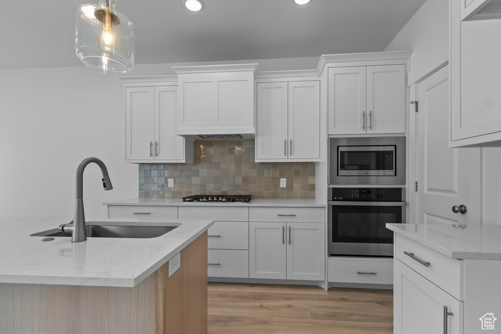 Kitchen with appliances with stainless steel finishes, a sink, decorative backsplash, white cabinets, and light stone counters